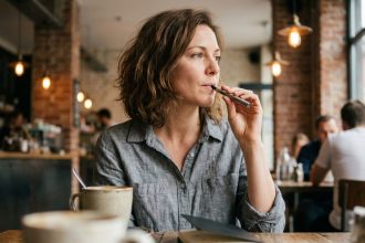 Femme ajustant son taux de nicotine dans une cigarette électronique dans un café urbain