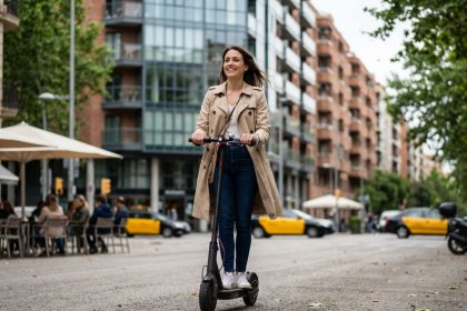 Jeune femme en trench et jeans sur scooter en ville