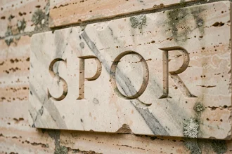 Tablette en marbre antique gravée des lettres SPQR, symbole de la République romaine, sur un mur en travertin patiné