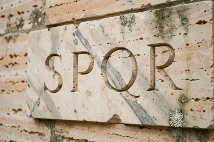 Tablette en marbre antique gravée des lettres SPQR, symbole de la République romaine, sur un mur en travertin patiné